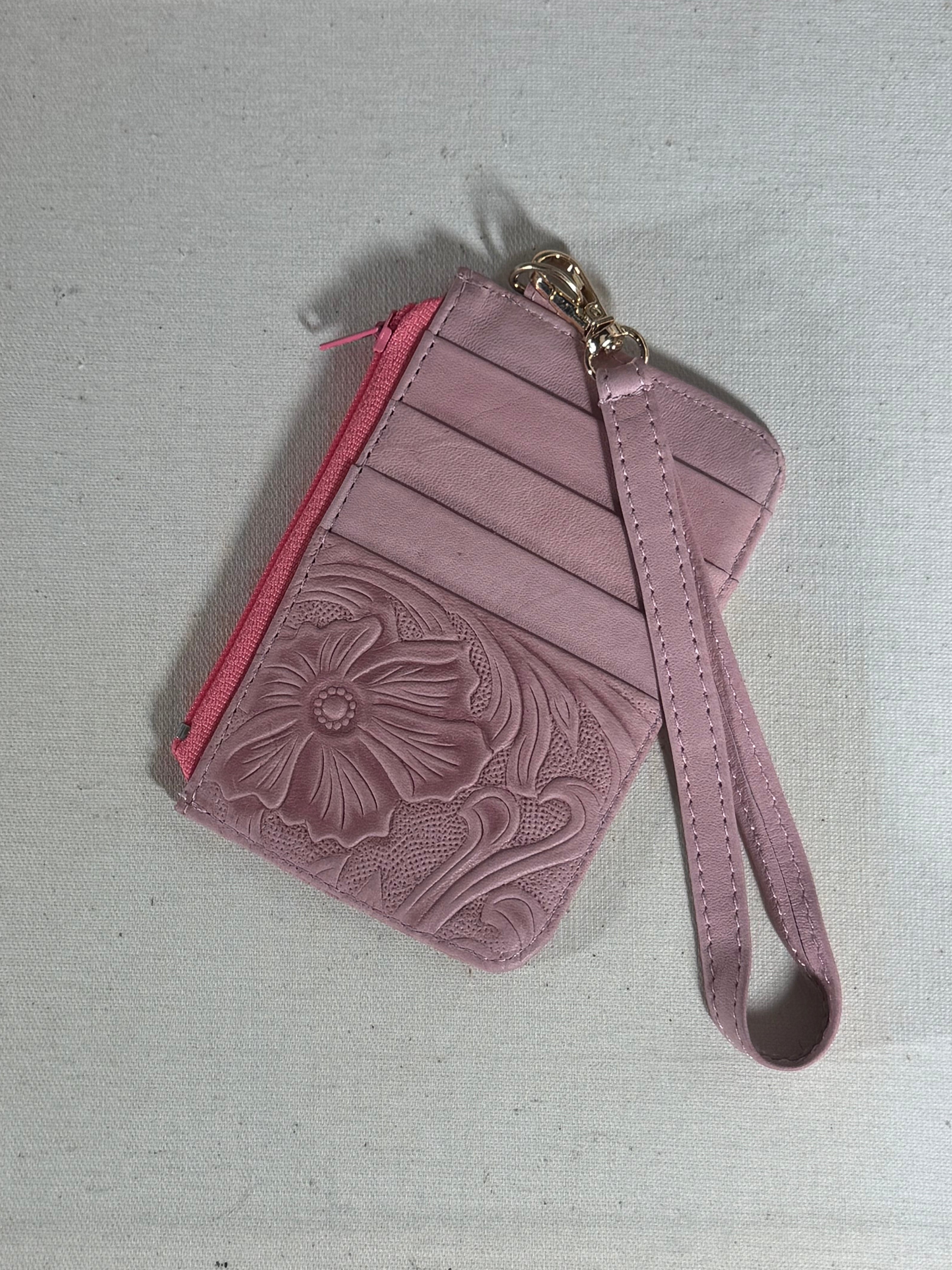 Pink leather wallet with floral embossing on a textured surface