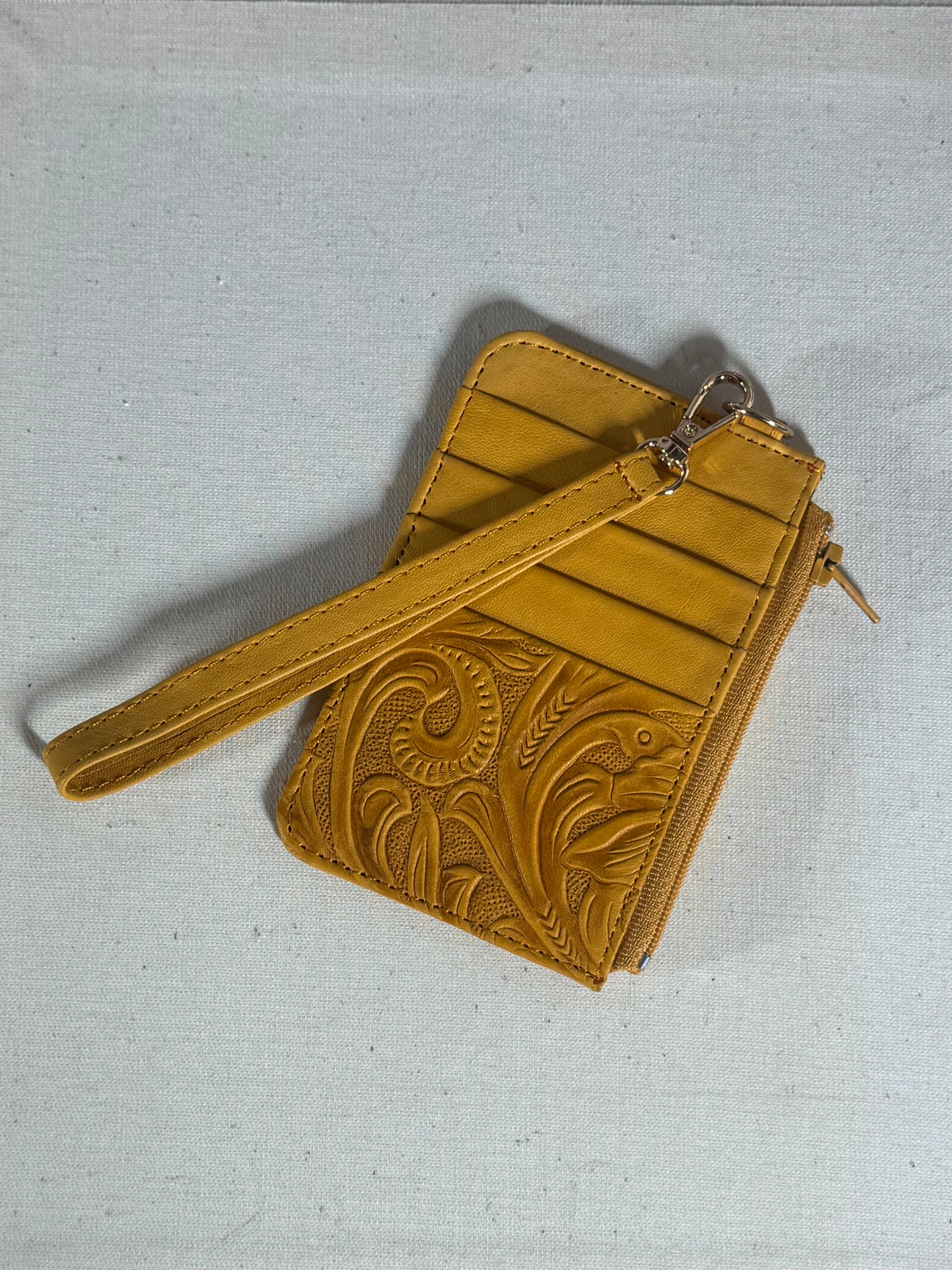 Yellow leather wristlet with intricate design on a textured surface